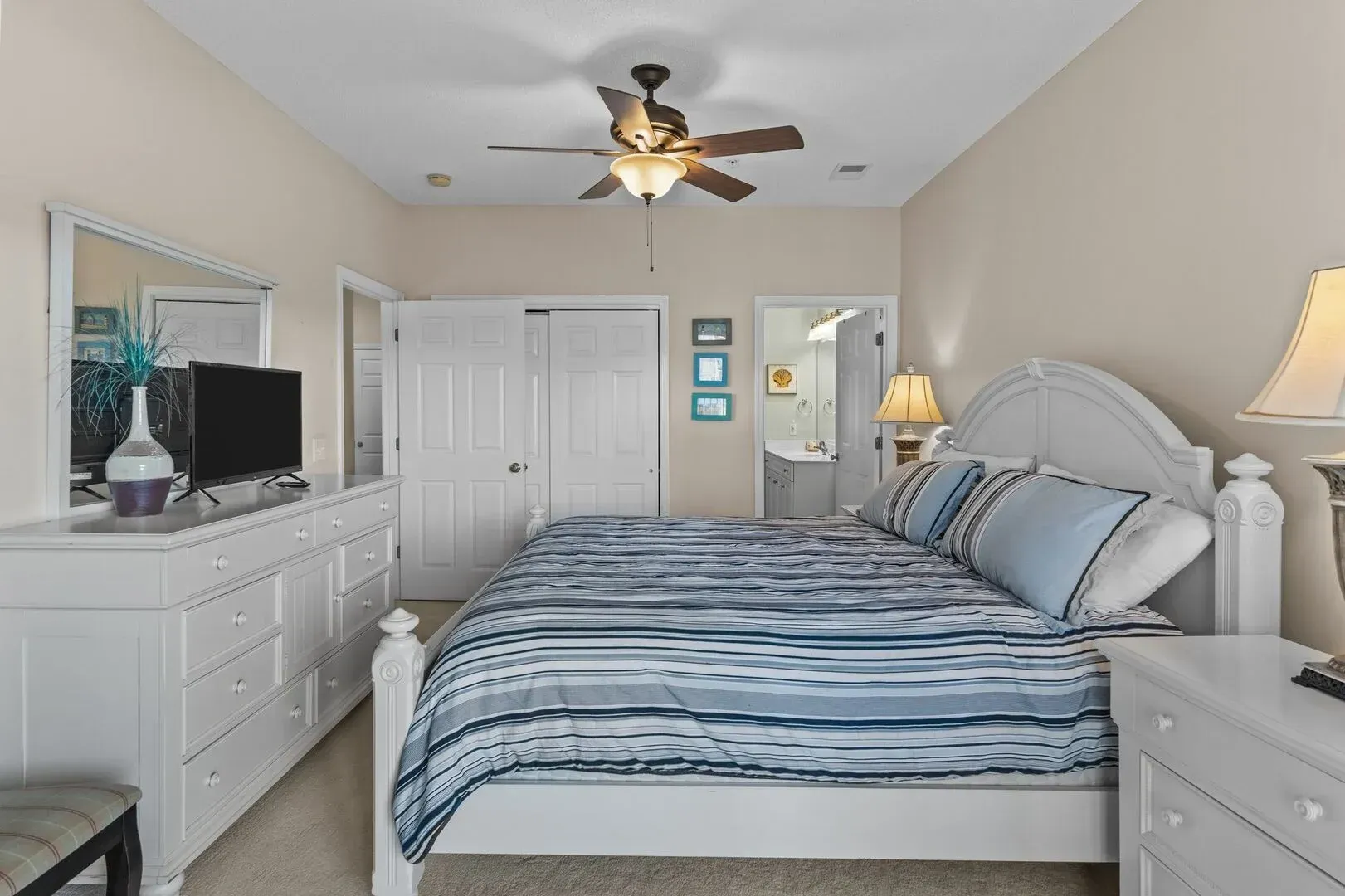 Bright bedroom with a white bed, blue bedding, dresser, mirror, and ceiling fan.