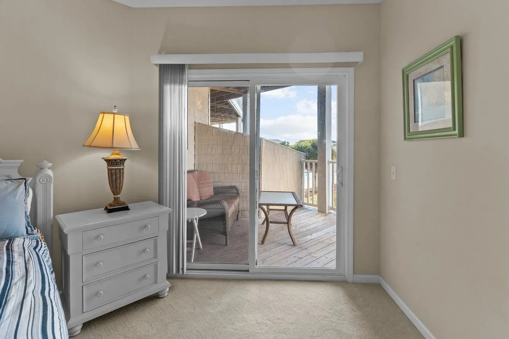 Bedroom with white dresser and lamp, opening to a sliding glass door and outdoor patio.