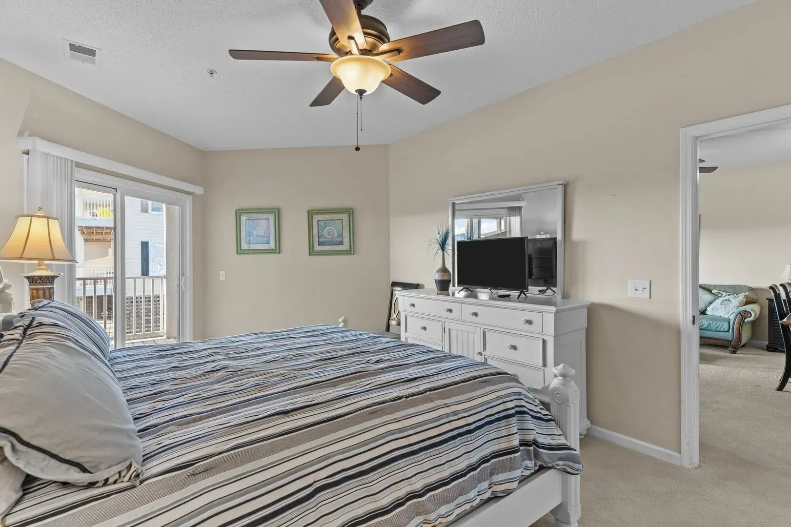 Bright bedroom with striped bedspread, ceiling fan, dresser, and open doorway to an adjoining room.