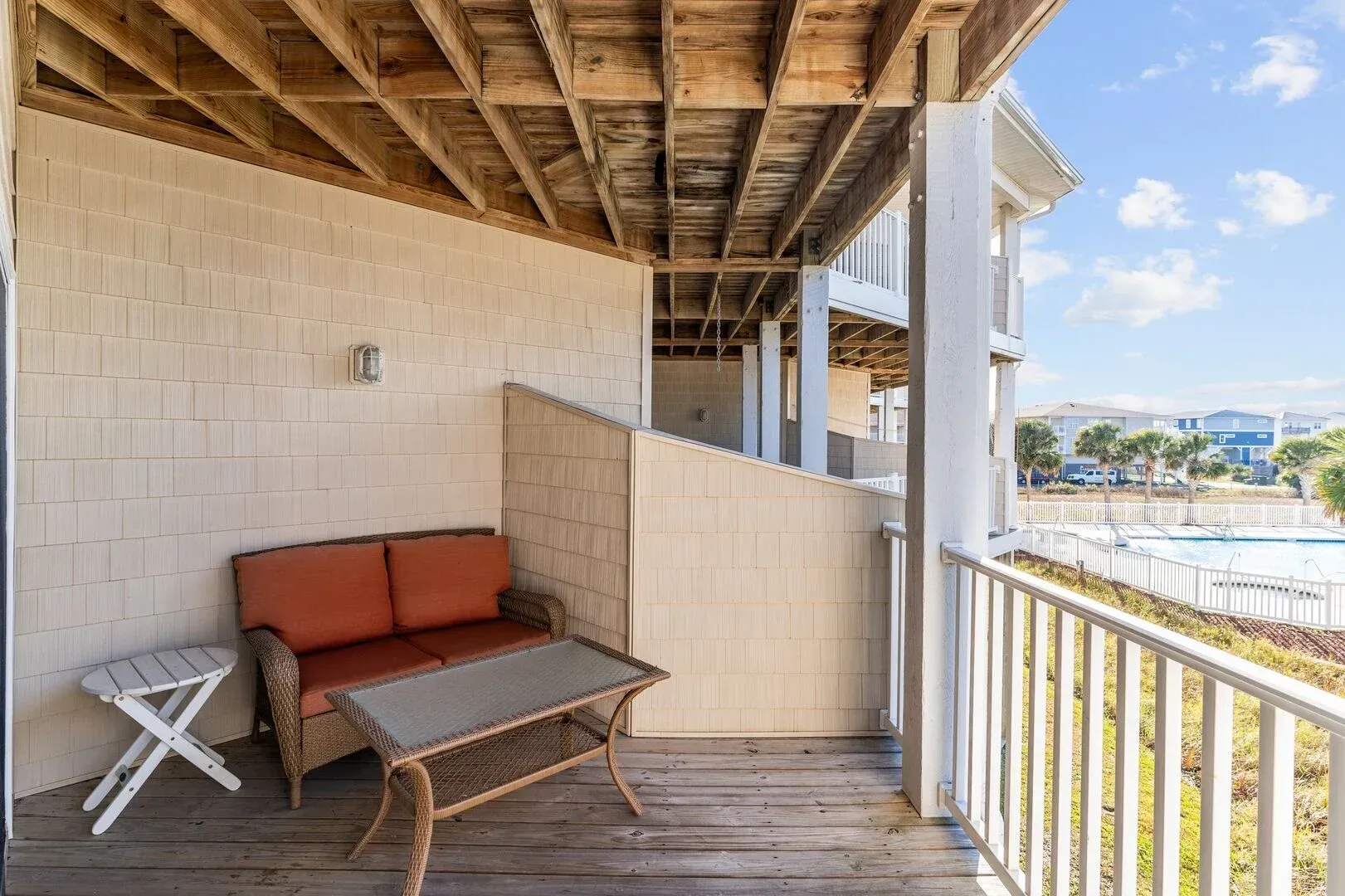Covered porch with cushioned bench, small table, and balcony railing overlooking the water
