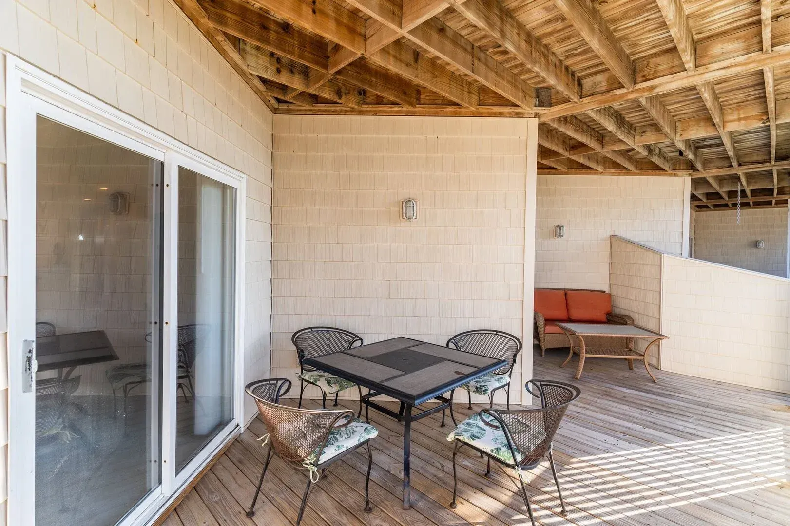 Covered patio with glass table and chairs, sliding door, and a sofa under a wood-beam ceiling.