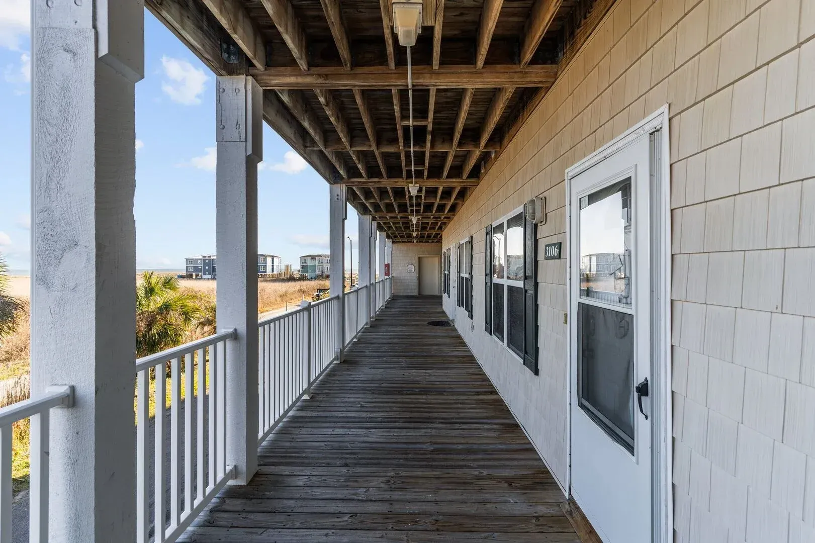 Wooden porch walkway with railing beside white building, leading into the distance under exposed beams.