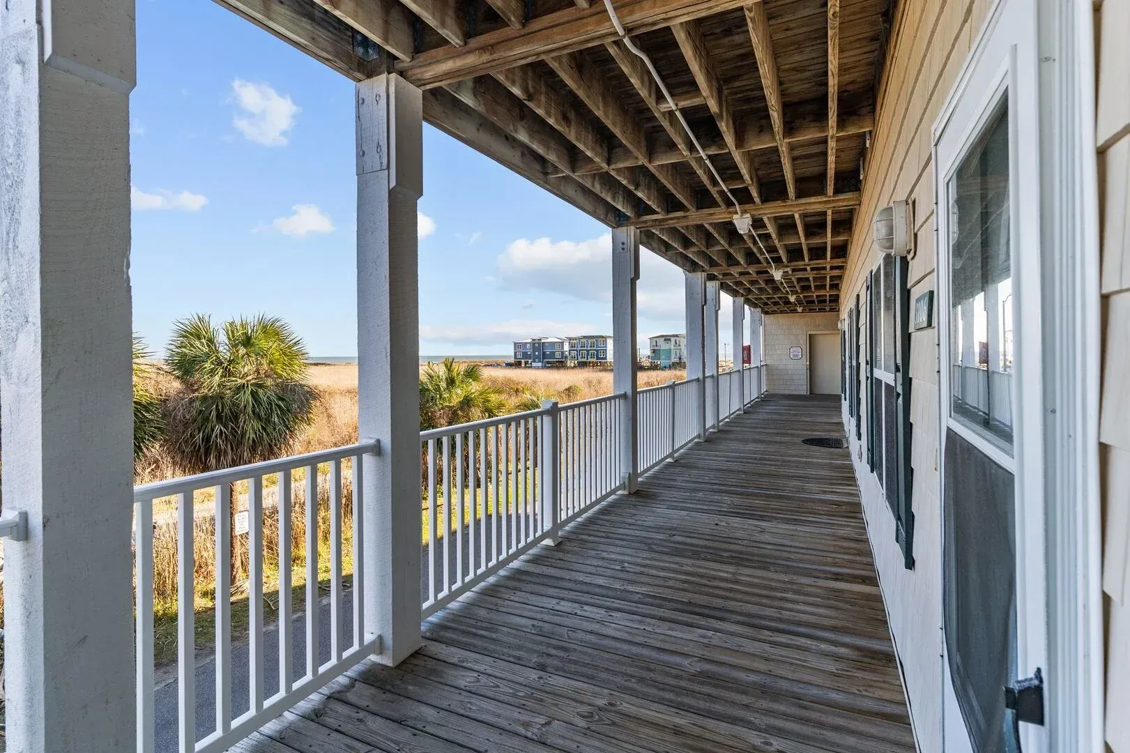 Empty wooden porch walkway with white railings and windows, overlooking a sunny landscape.