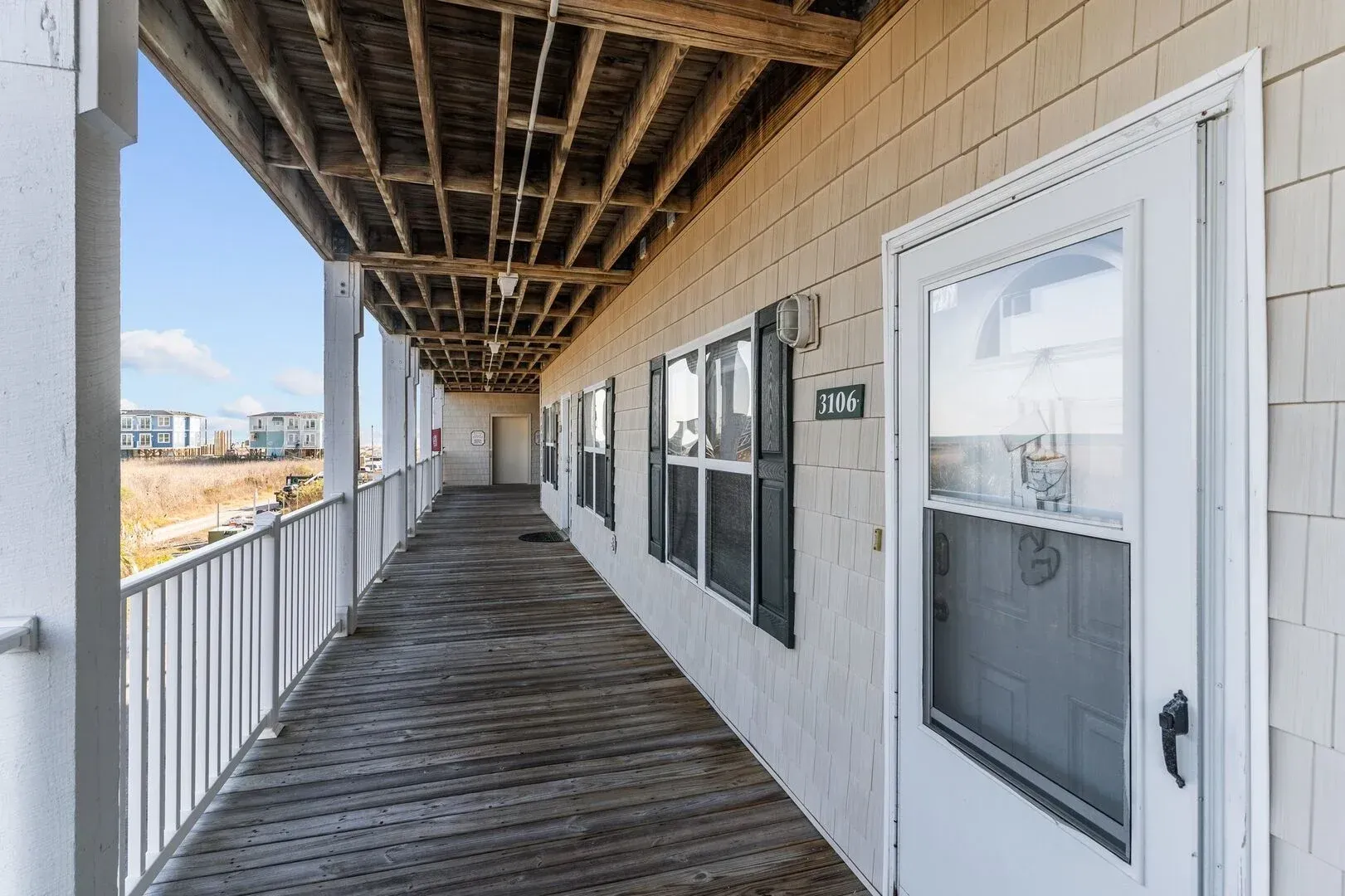 Covered apartment walkway with white doors, windows, and wooden flooring under exposed beams
