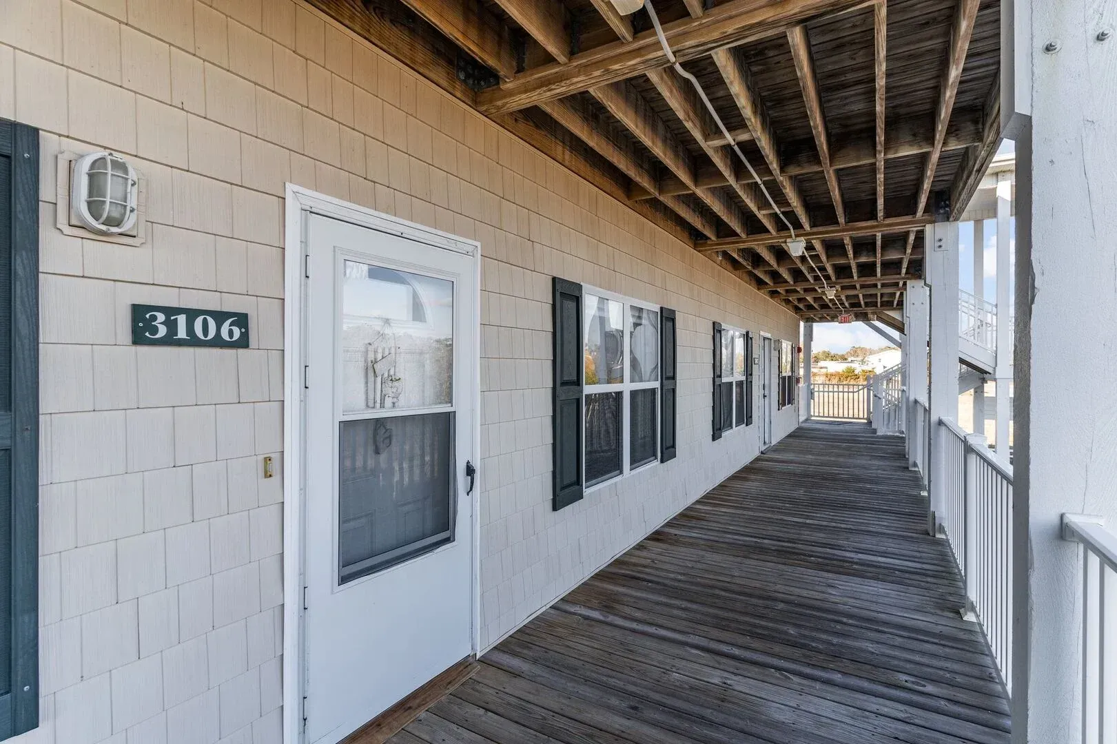 Exterior walkway of a building with white doors and windows, wooden railing, and room number 3106.