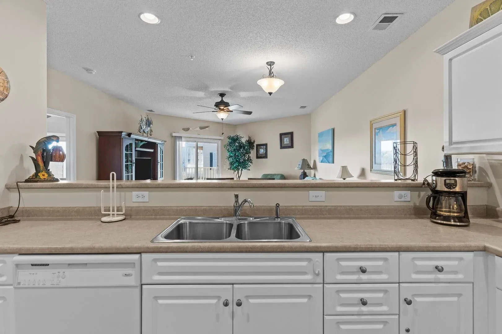 Kitchen view over a sink to a bright open living area with white cabinets and beige countertops