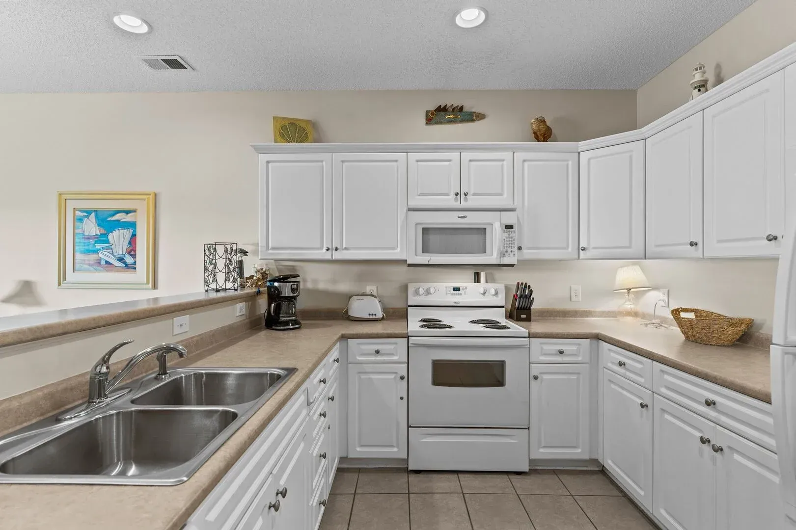 Bright white U-shaped kitchen with white cabinets, stainless sink, stove, and microwave.
