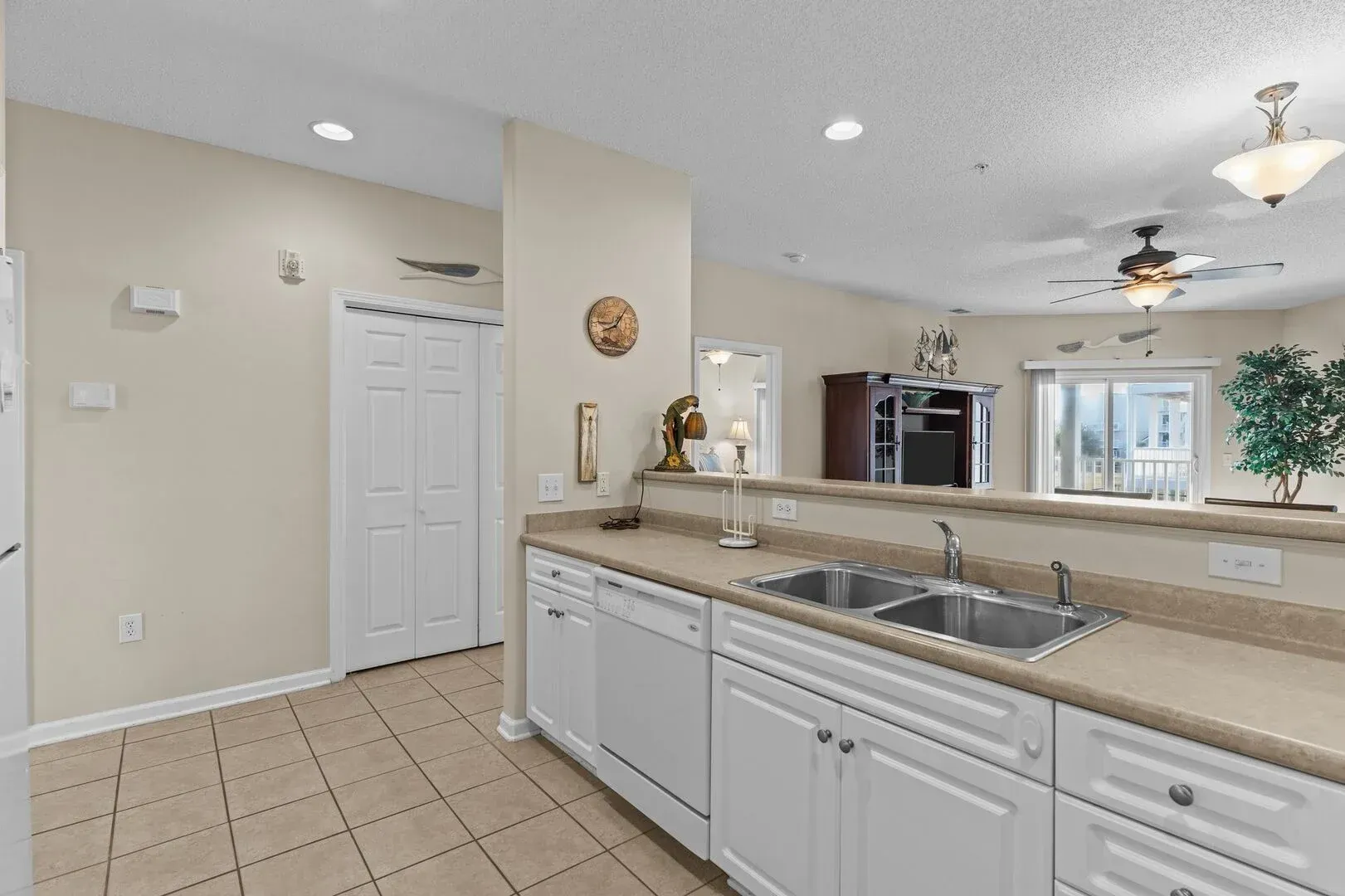 Bright kitchen with white cabinets, beige tile floor, island counter, and stainless steel sink.