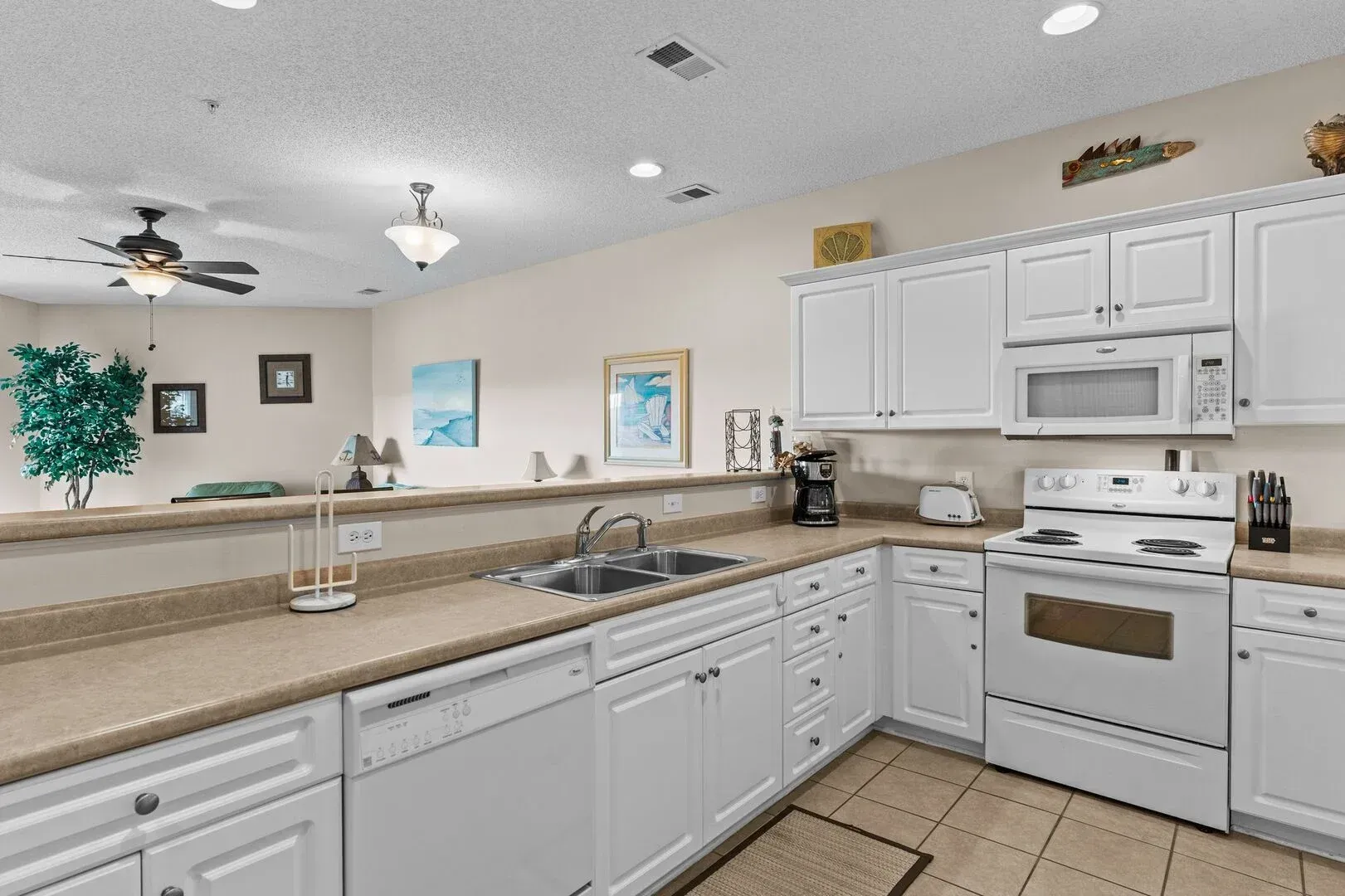 Bright white kitchen with tan countertops, white cabinets, sink, stove, and tiled floor.