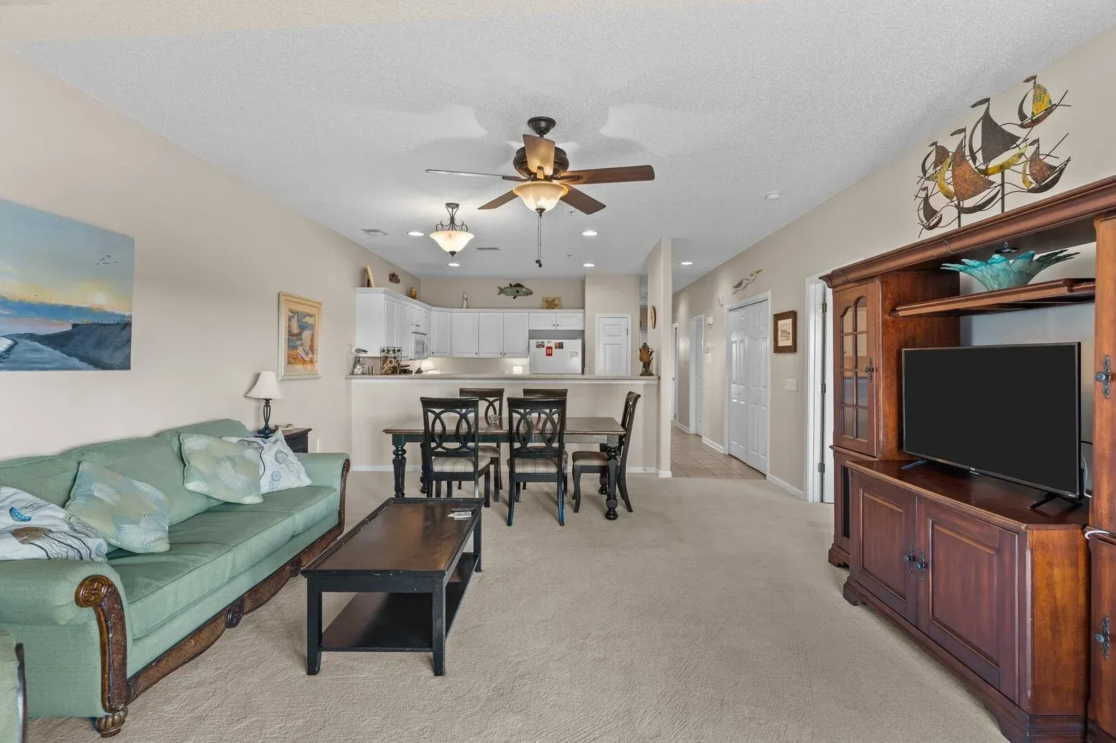 Bright living room with green sofa, dining table, ceiling fan, and TV cabinet in open layout.