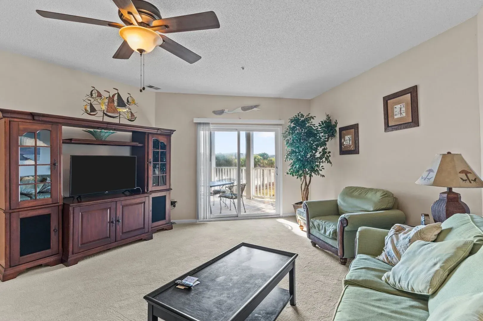 Bright living room with green sofas, TV cabinet, coffee table, and sliding glass doors to a patio.