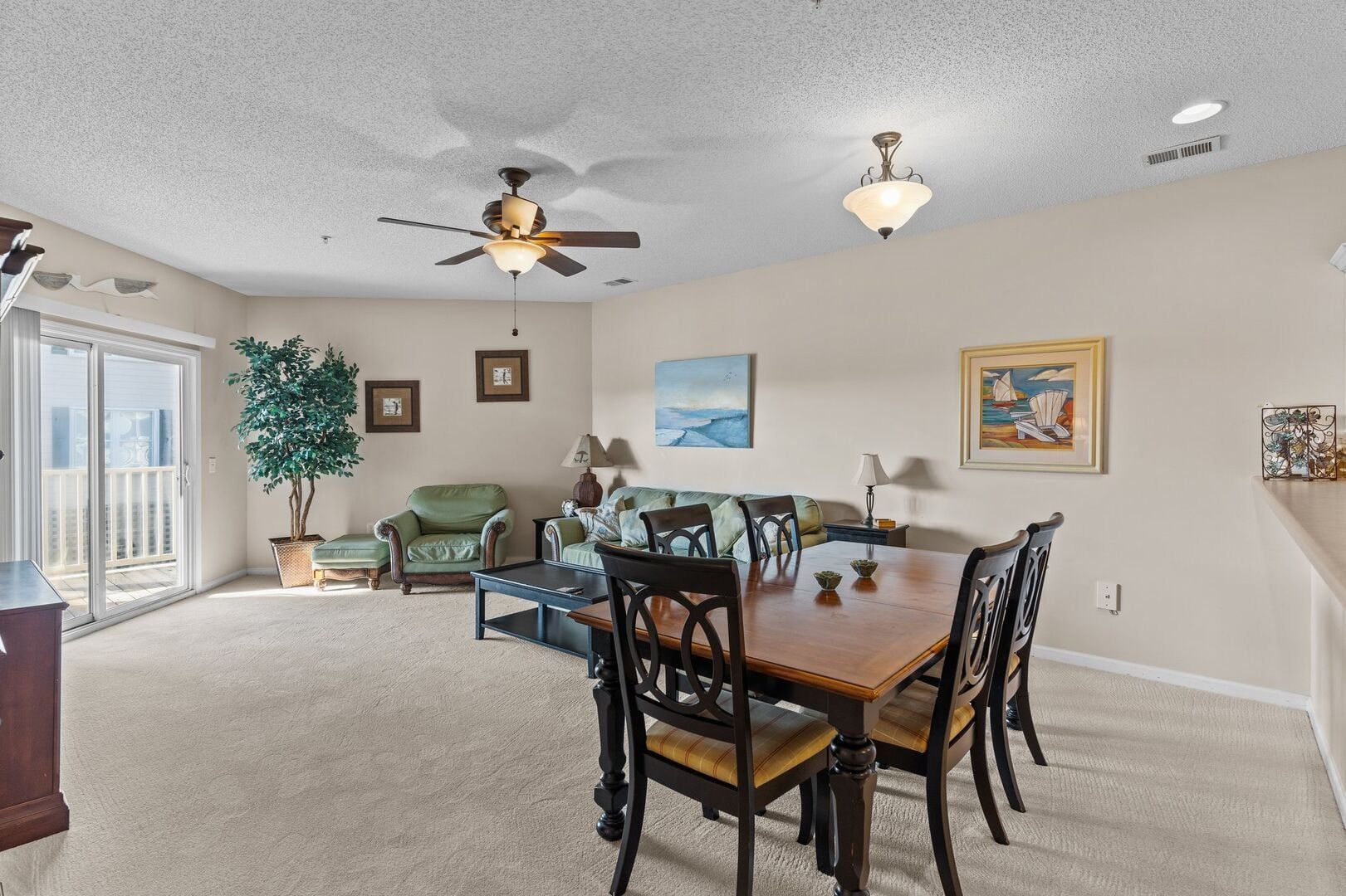 Bright dining and living room with dark wood table, green chairs, beige walls, and ceiling fan
