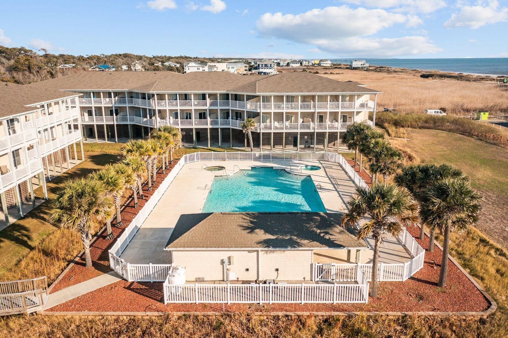 Aerial view of a resort hotel with a large turquoise pool, palm trees, and desert landscape beyond.