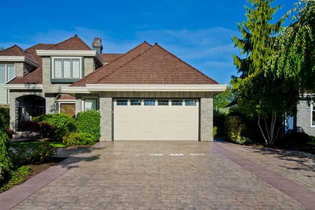 Suburban house with beige garage door, red-tiled roof, and brick driveway under a blue sky