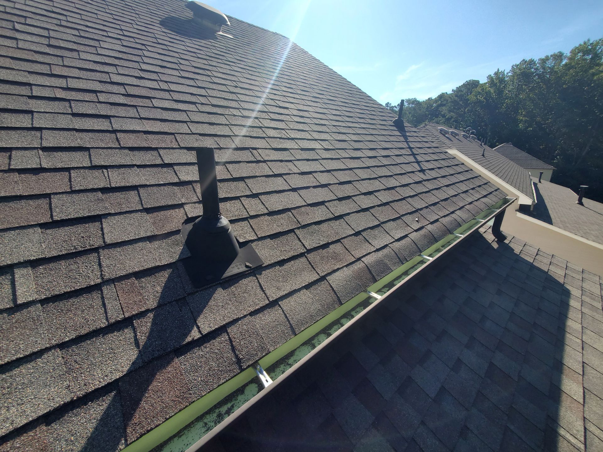 Brown shingled roof with gutter and vent pipes on a sunny day.