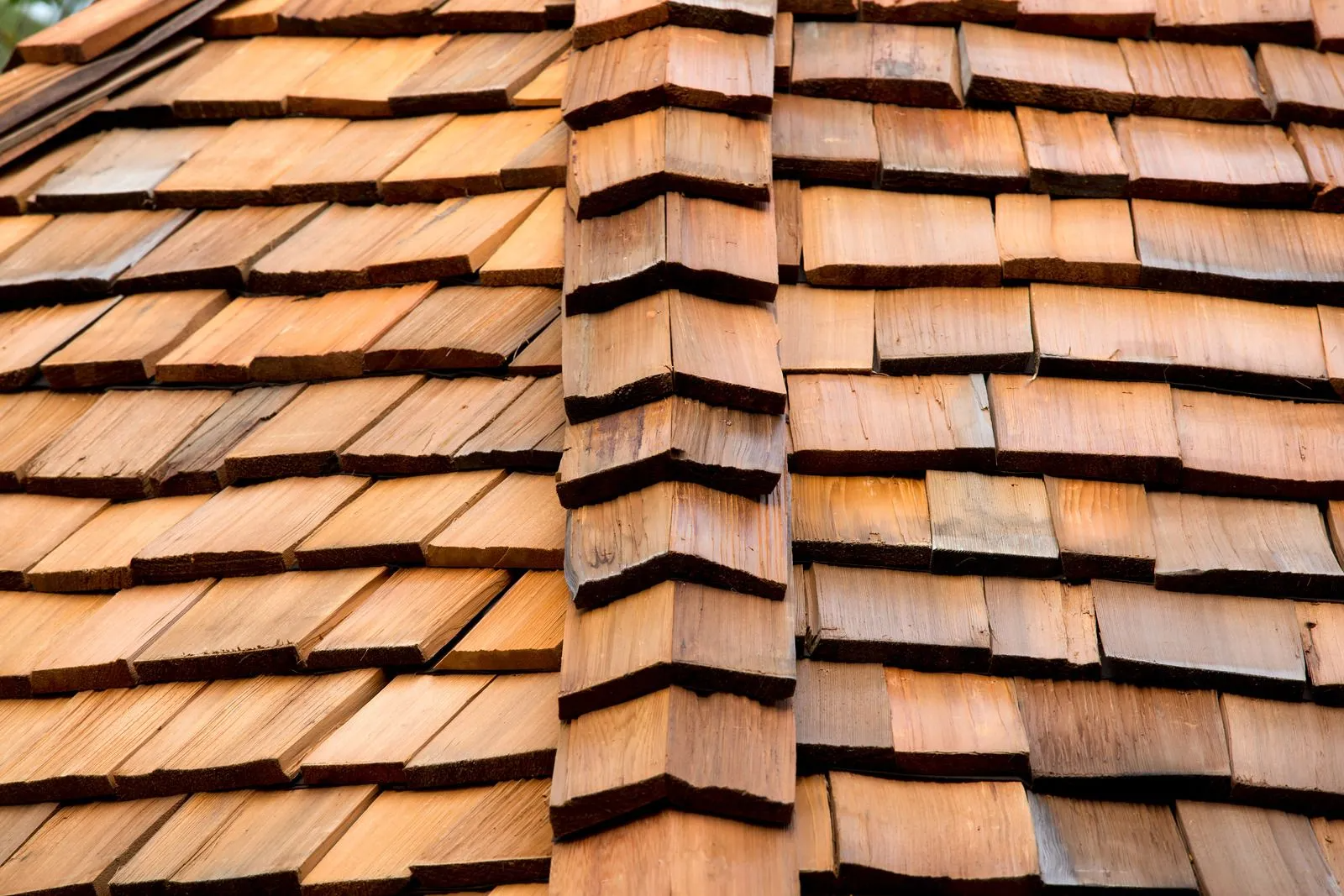 Close-up of a brown cedar shingle roof with a vertical ridge line, showcasing texture and pattern.