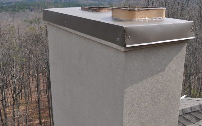 Chimney with metal cap and two openings on a roof, brown and gray tones, outdoor setting.