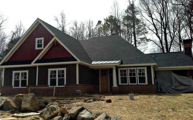 Brown and red craftsman-style home with brick foundation, windows, and a dark roof; set among trees.