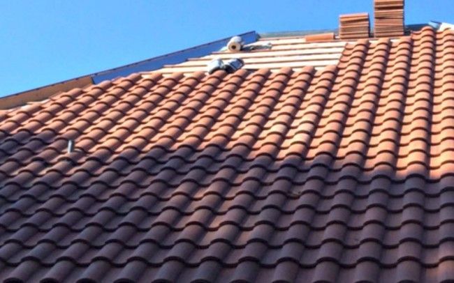 Roof with red clay tiles under clear blue sky, partially undergoing repair by workers.