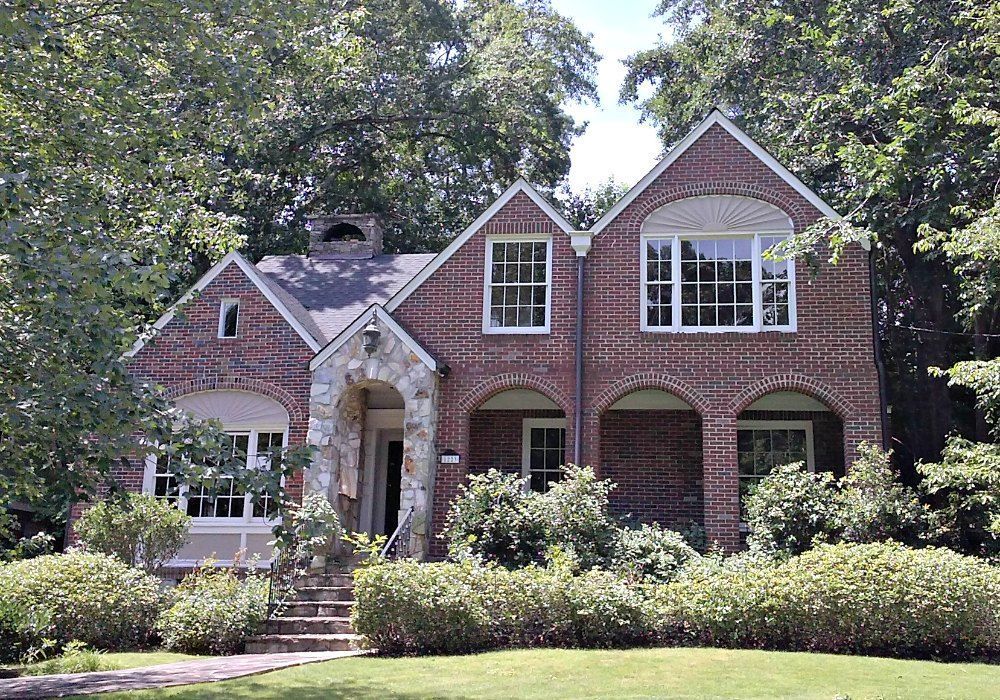 Brick house with arched entry, large windows, and green lawn.