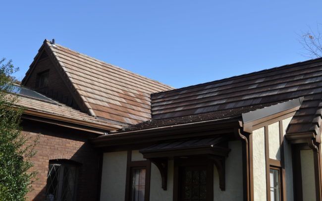 Tudor style building with brown roof tiles, light tan stucco, and dark brown trim against a blue sky.