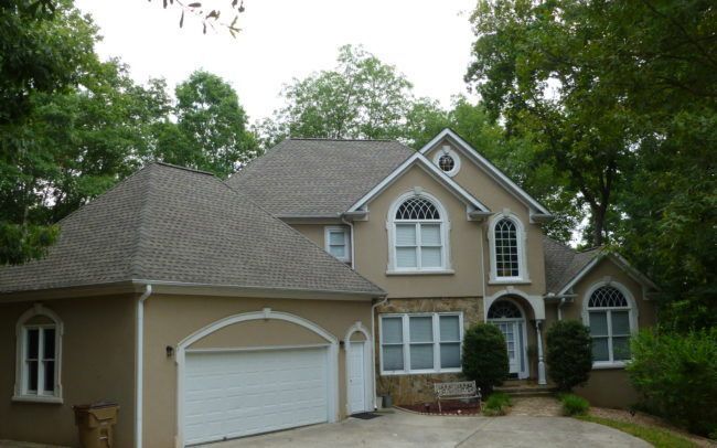 Beige house with arched windows, white trim, and a garage door, nestled amongst trees.
