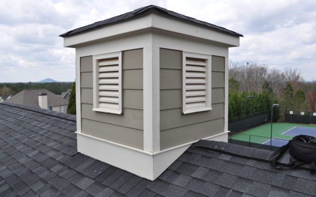Square roof vent with beige siding, white trim, and horizontal louvers on a shingle roof.
