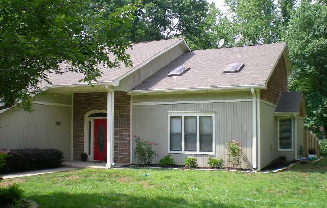 A beige house with a red door, windows, and a green lawn.