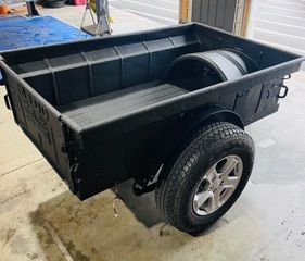 Black trailer with truck bed design, black tires, and silver rims.