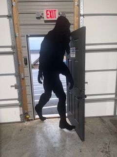 Silhouette of a person carrying a door through an exit, beneath an EXIT sign. Industrial setting.