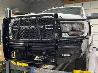 Black heavy-duty truck bumper with grill guard on a white Ram truck.