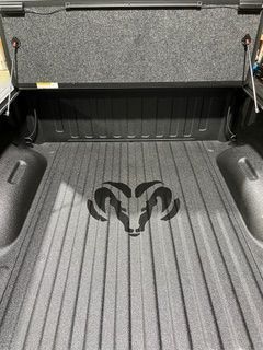 Ram truck bed with bedliner and Ram logo, with tonneau cover open.