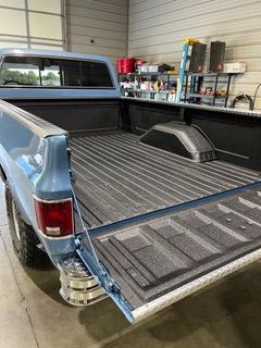 Blue pickup truck with open tailgate in a garage, showcasing a bedliner.