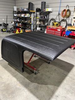 Black Jeep hardtop on a red rolling stand in a workshop.