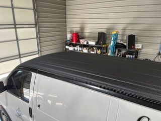 White van's black roof in a garage, with shelves of items against a corrugated metal wall.