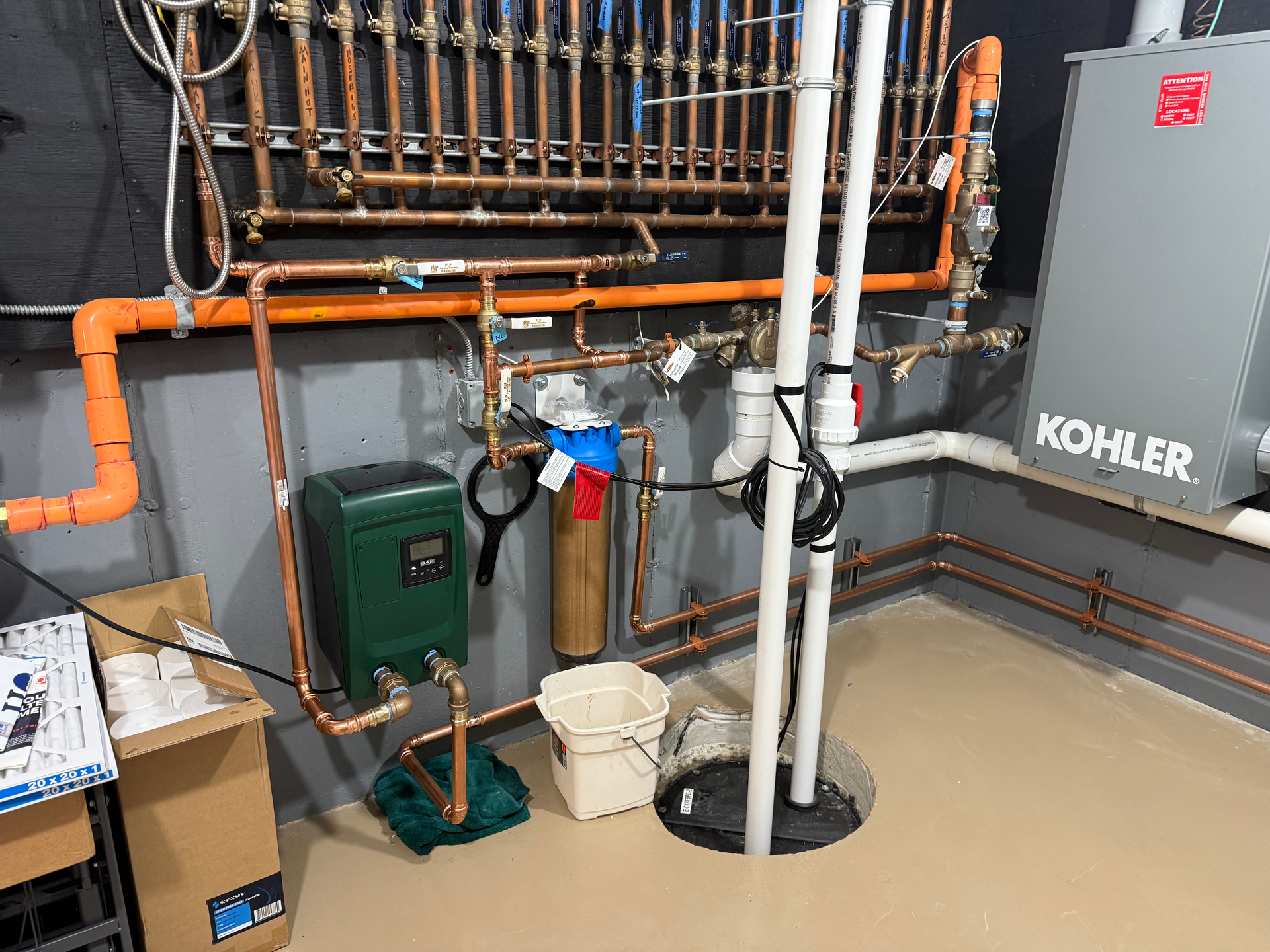 Basement utility room with orange piping, pump, gray boiler, and white water heater рядом a floor drain.
