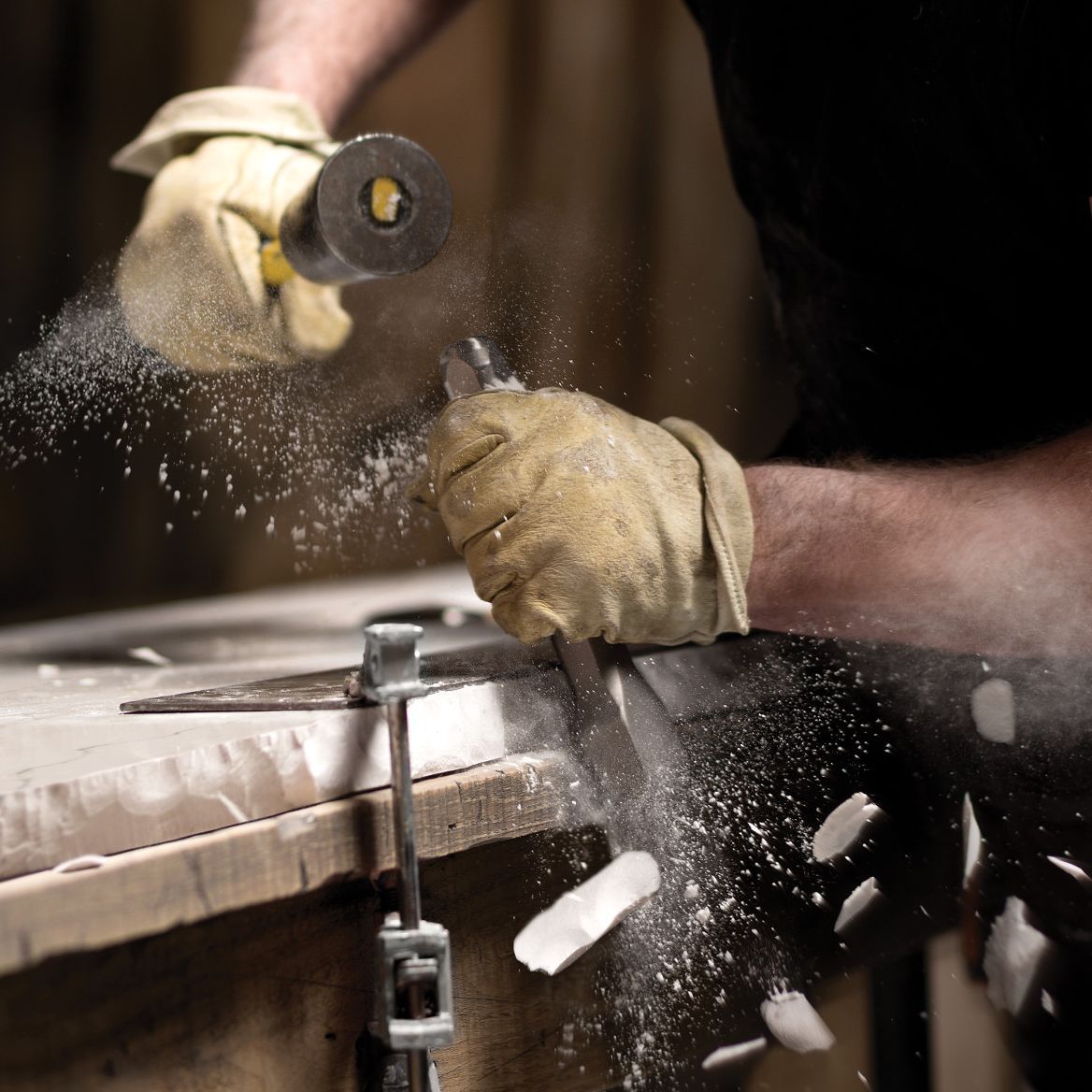 A man wearing gloves is using a grinder on a piece of metal