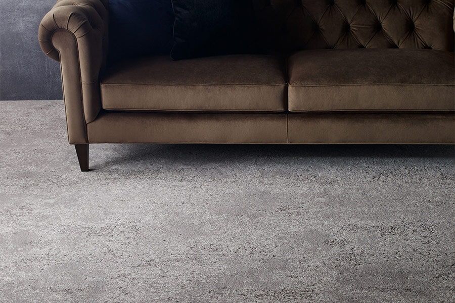 A brown couch is sitting on a gray rug in a living room.