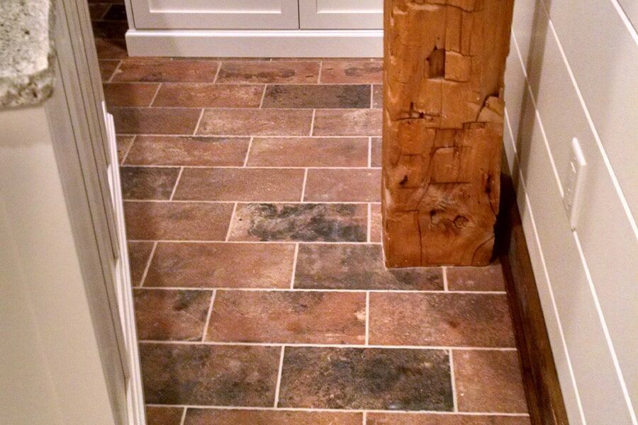 A tiled floor in a kitchen with a wooden post in the corner.