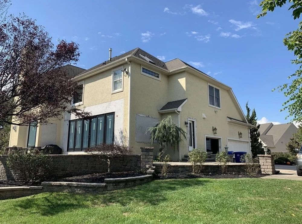 Two-story house with stucco exterior and folding doors, blue sky background.