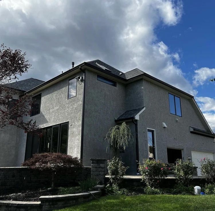 Gray stucco house with black framed windows, a dark roof, and cloudy sky.