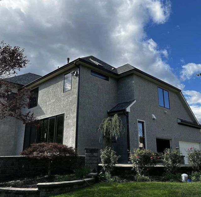 Gray stucco house with black framed windows, a dark roof, and cloudy sky.