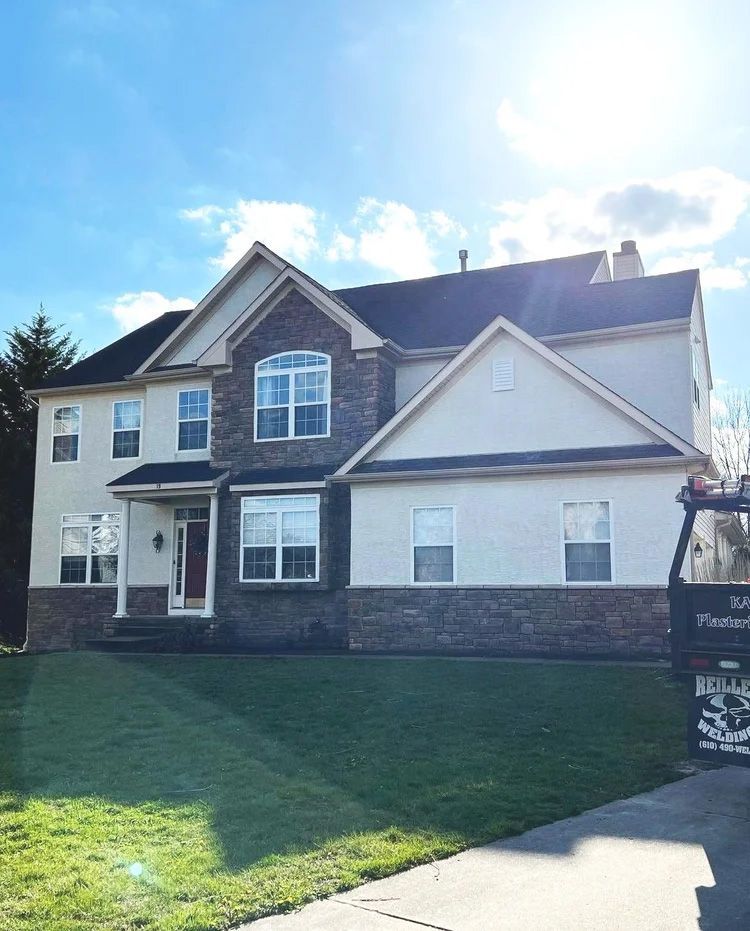Two-story house with stone and light-colored siding, green lawn, blue sky.