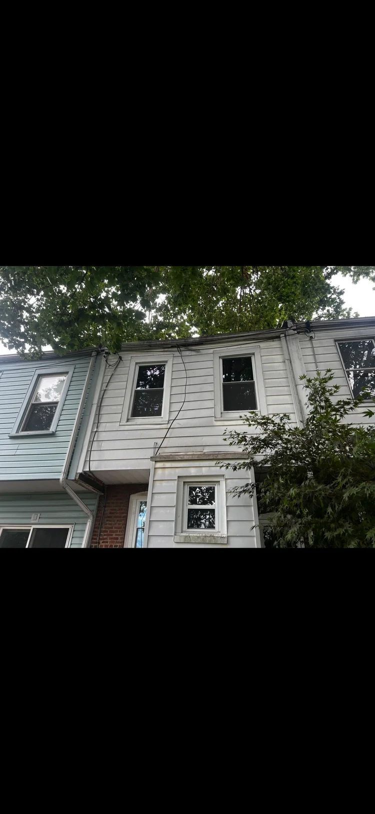 Weathered two-story house with peeling paint, several windows, and surrounding trees.