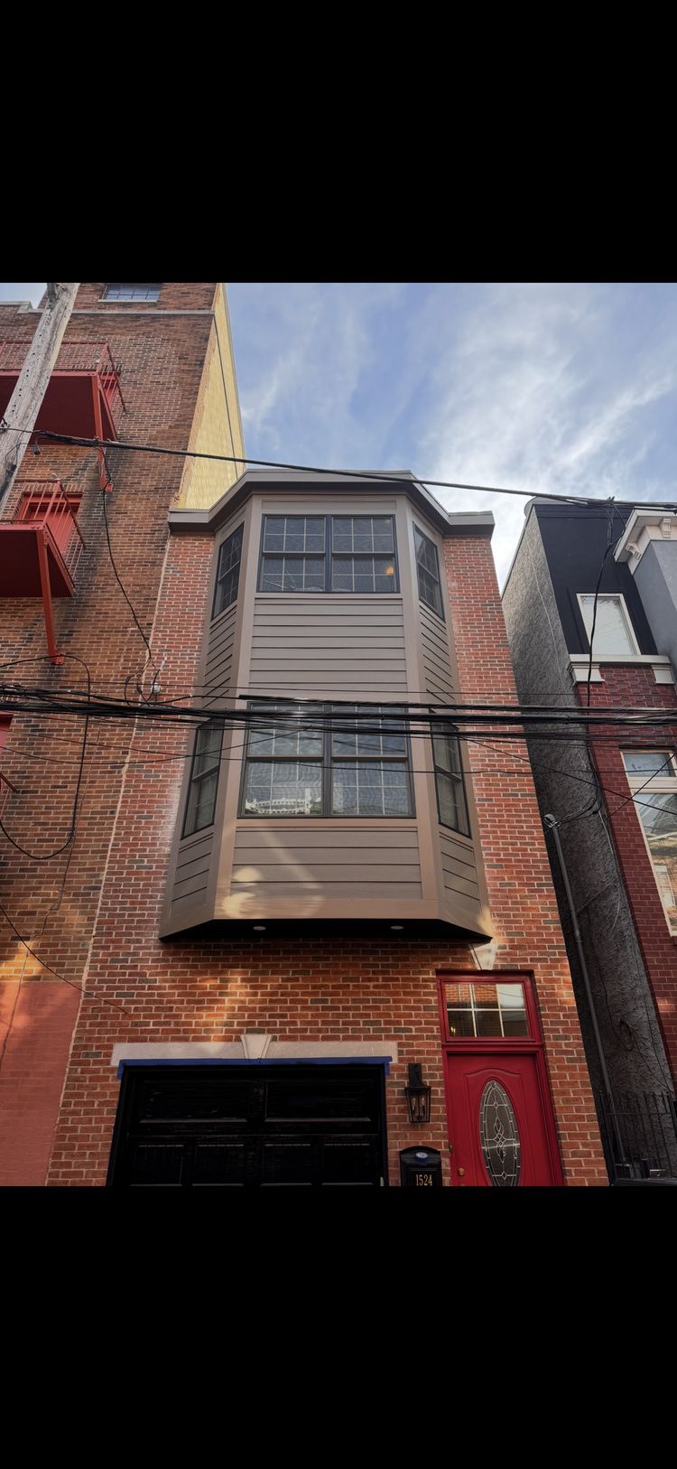 Brick building with a three-sided bay window, black garage door, and red front door.