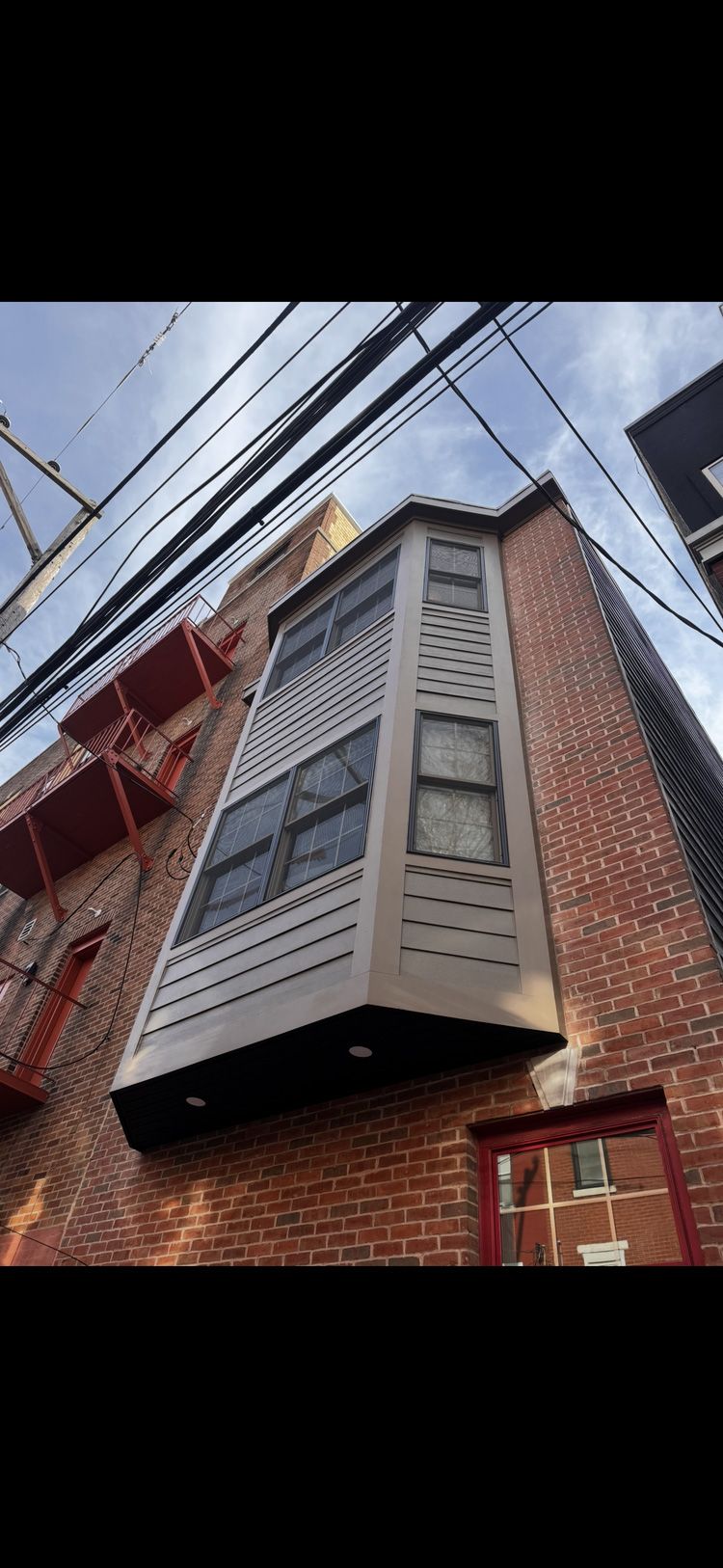 Brick building with a bay window and a fire escape. Wires are overhead.