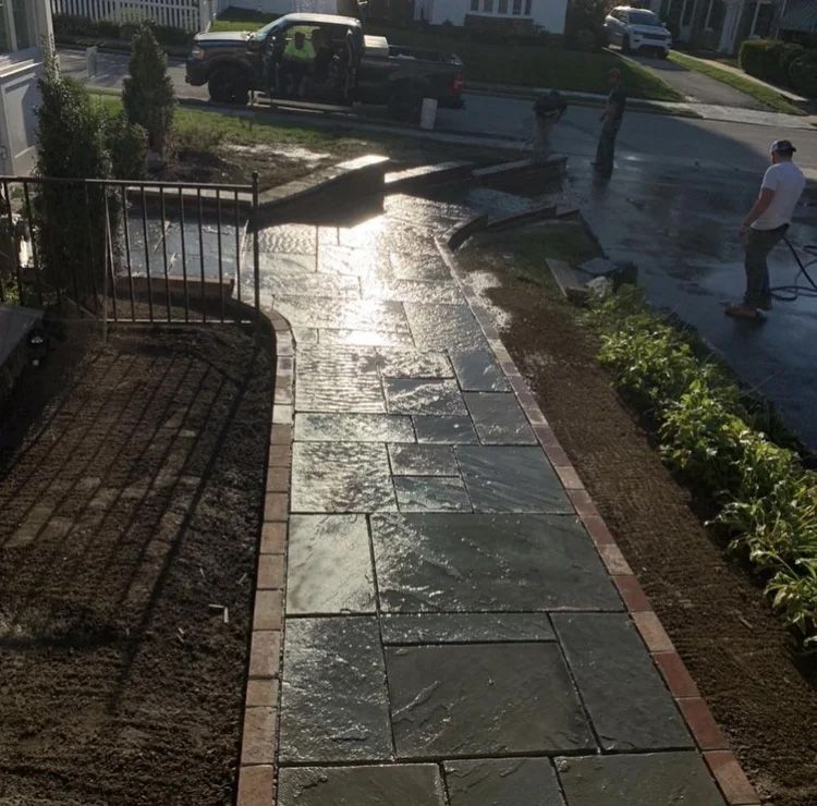 Wet stone walkway being cleaned; person using a power washer.