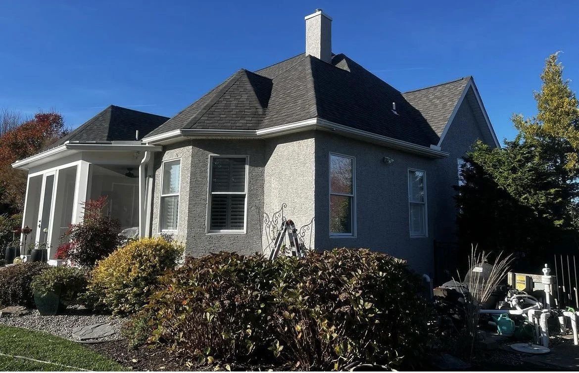 Gray stucco house with dark gray roof, chimney, and shutters. Landscaping in front.