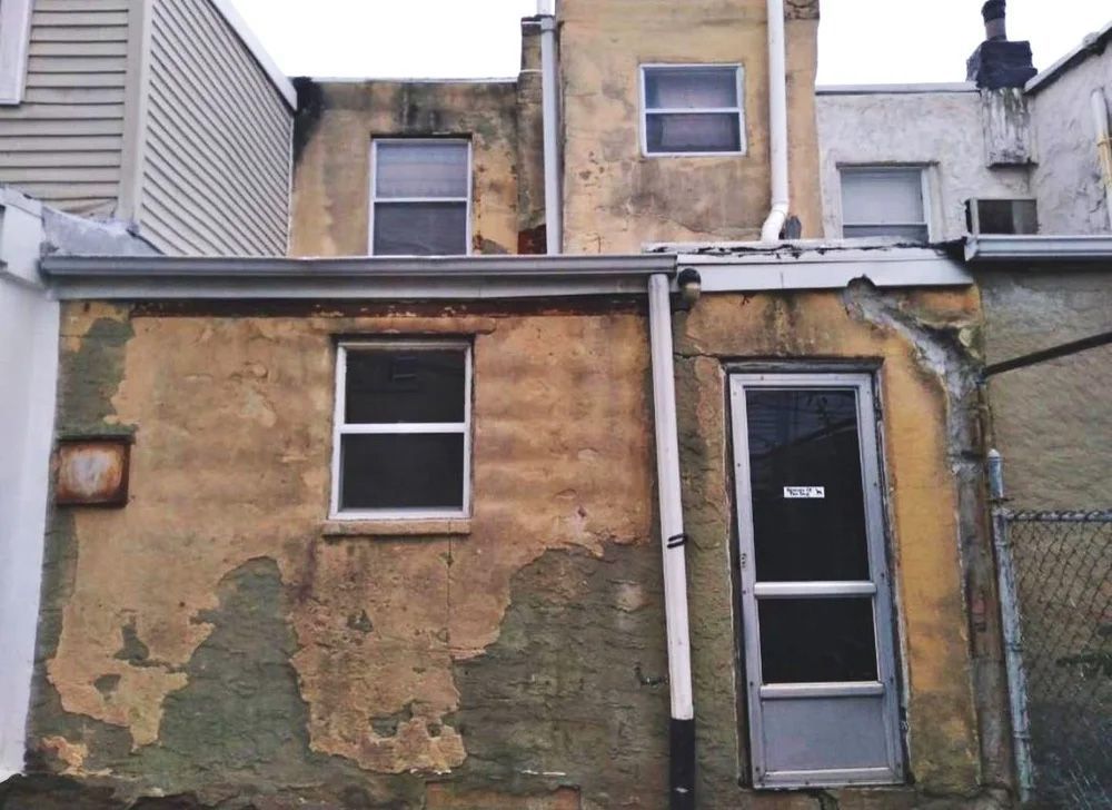 Exterior view of a weathered building with peeling paint. A door and windows are visible.