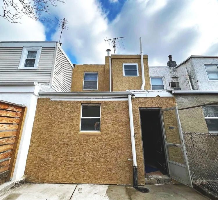 Backyard view of three connected tan buildings, two with antennas, and open doorway.